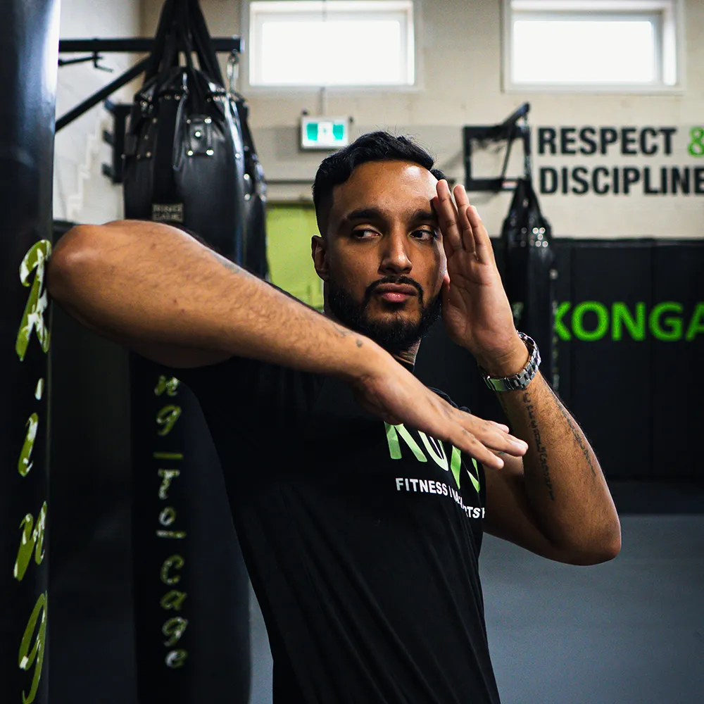 Coach demonstrating an elbow strike beside a punching bag