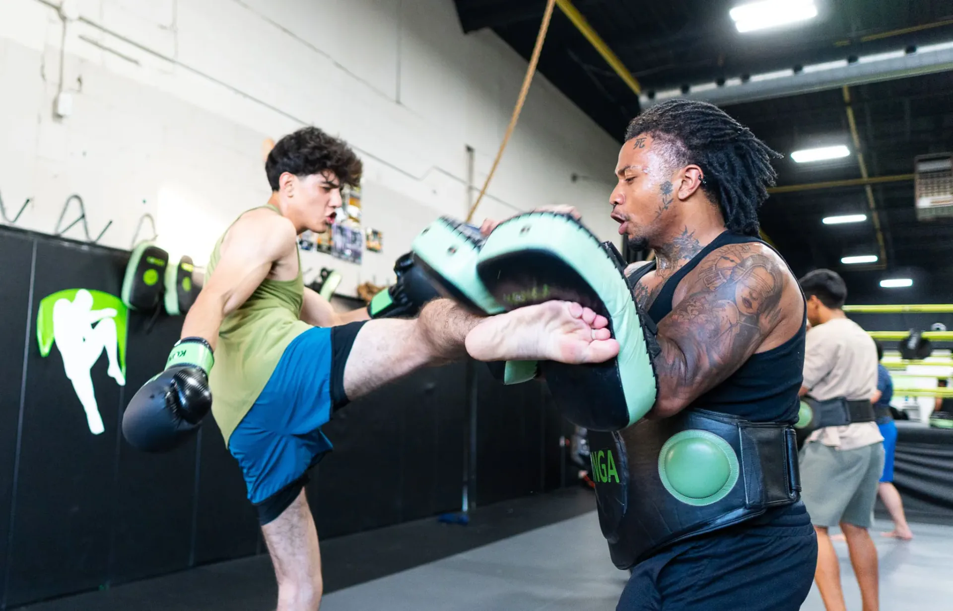 Muay Thai student kicking pads held by a coach