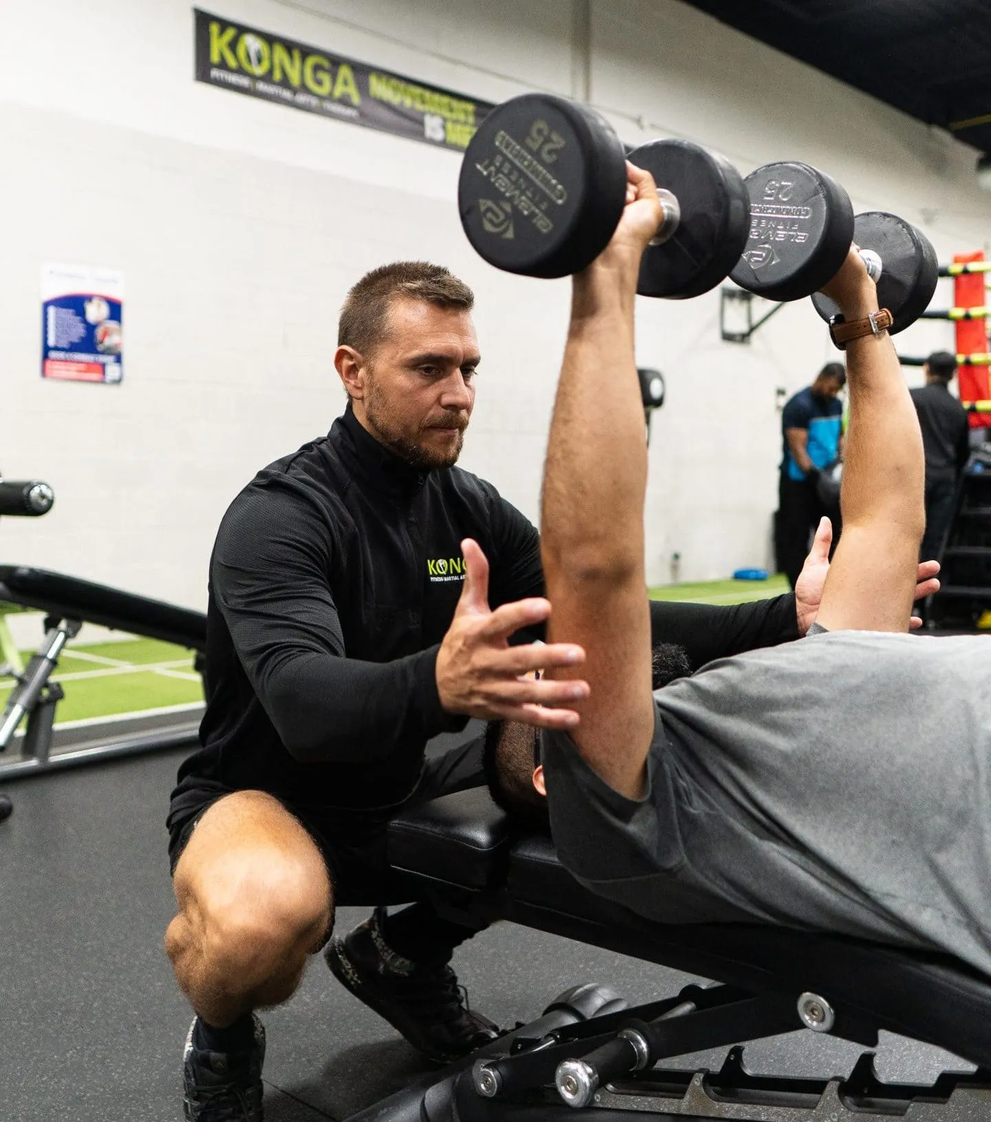Trainer spotting a member's dumbbell bench press
