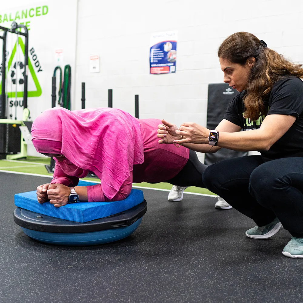 Trainer guiding a member through an exercise on a balance trainer