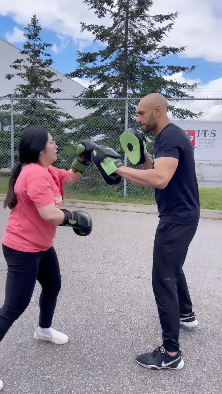 Coach holding focus mitts for a woman training outdoors