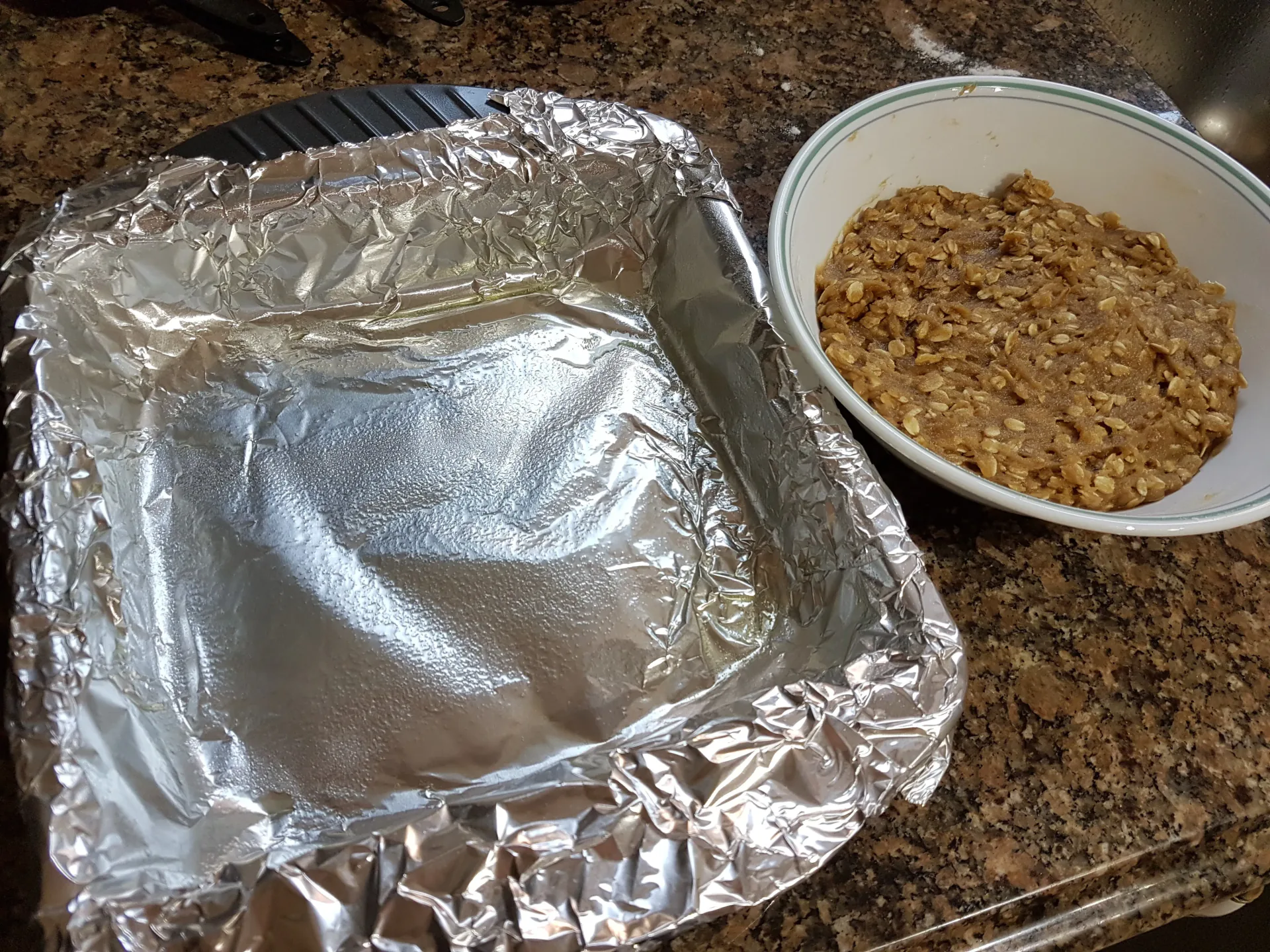 Foil-lined baking pan beside a bowl of oat mixture