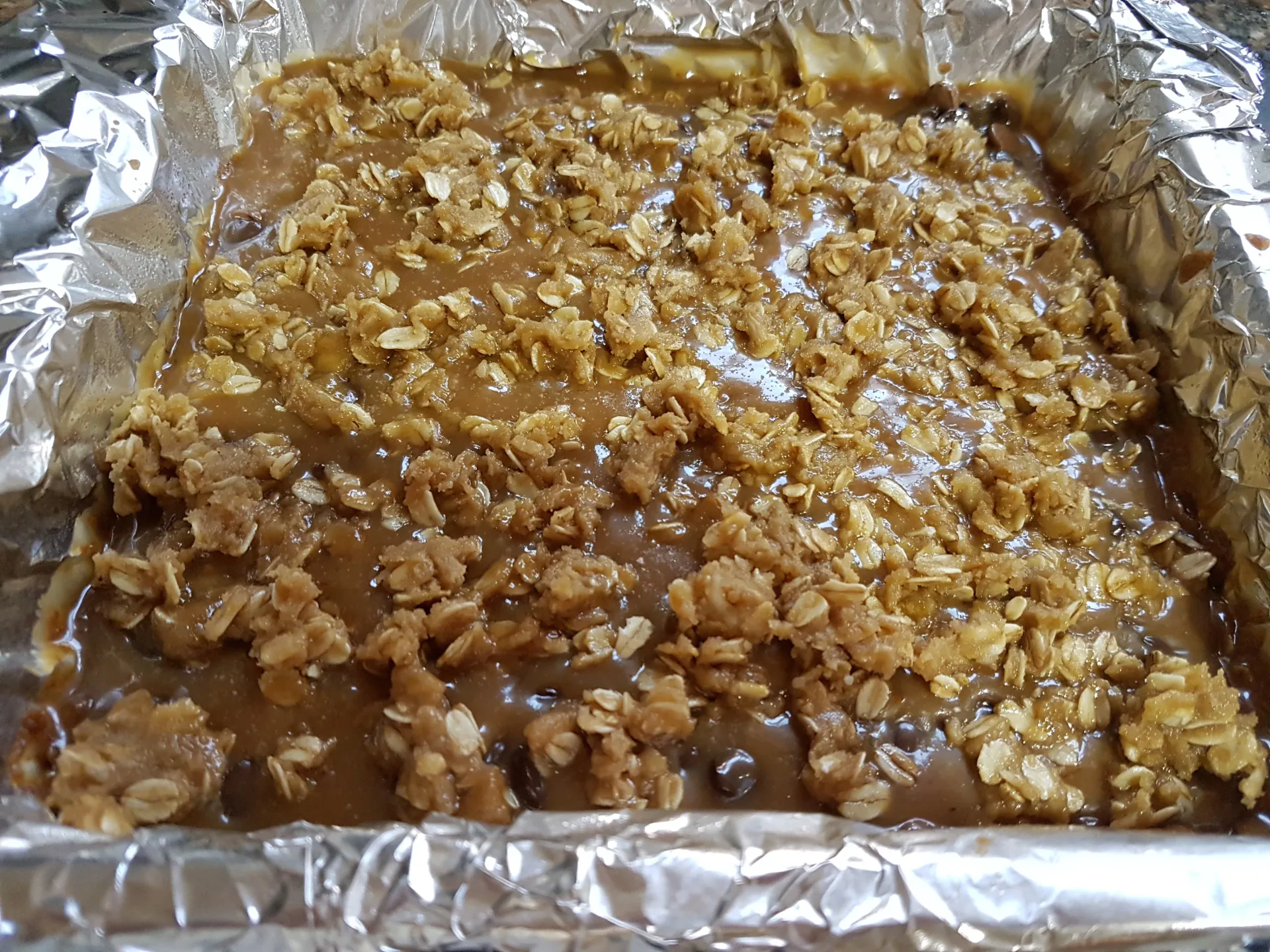 Carmelita mixture topped with oat crumbs in a foil-lined pan