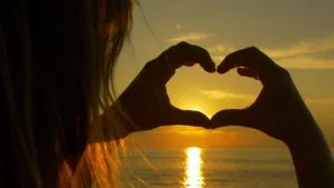 Hands forming a heart shape against a sunset