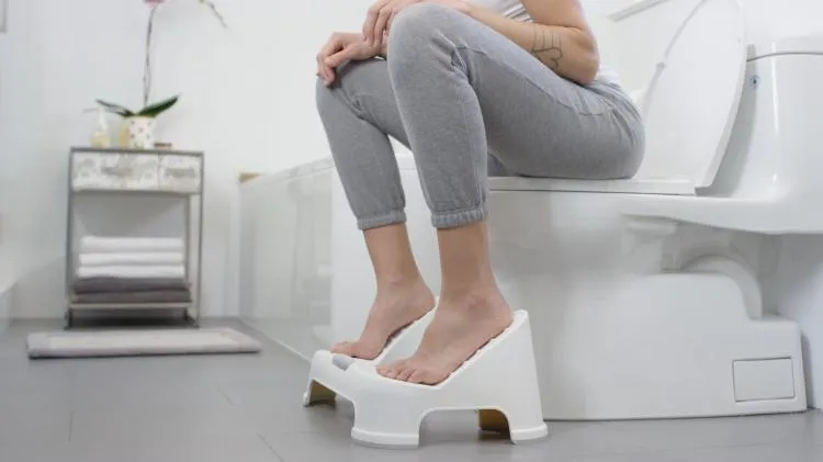 Person using a footstool while seated on a toilet