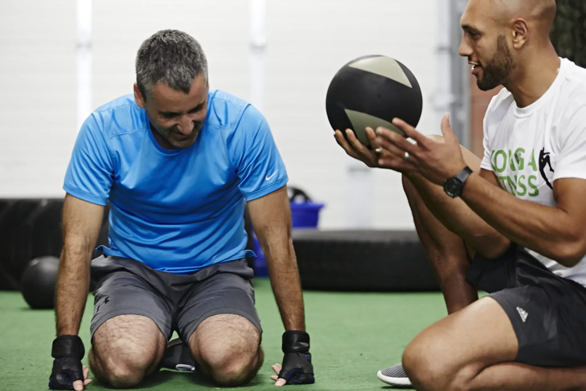 Trainer holding a medicine ball beside a seated member with dumbbells
