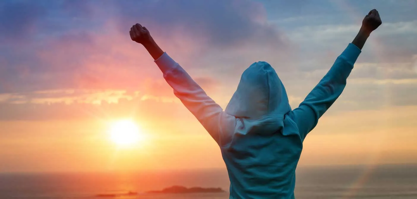 Person raising both arms toward a sunset
