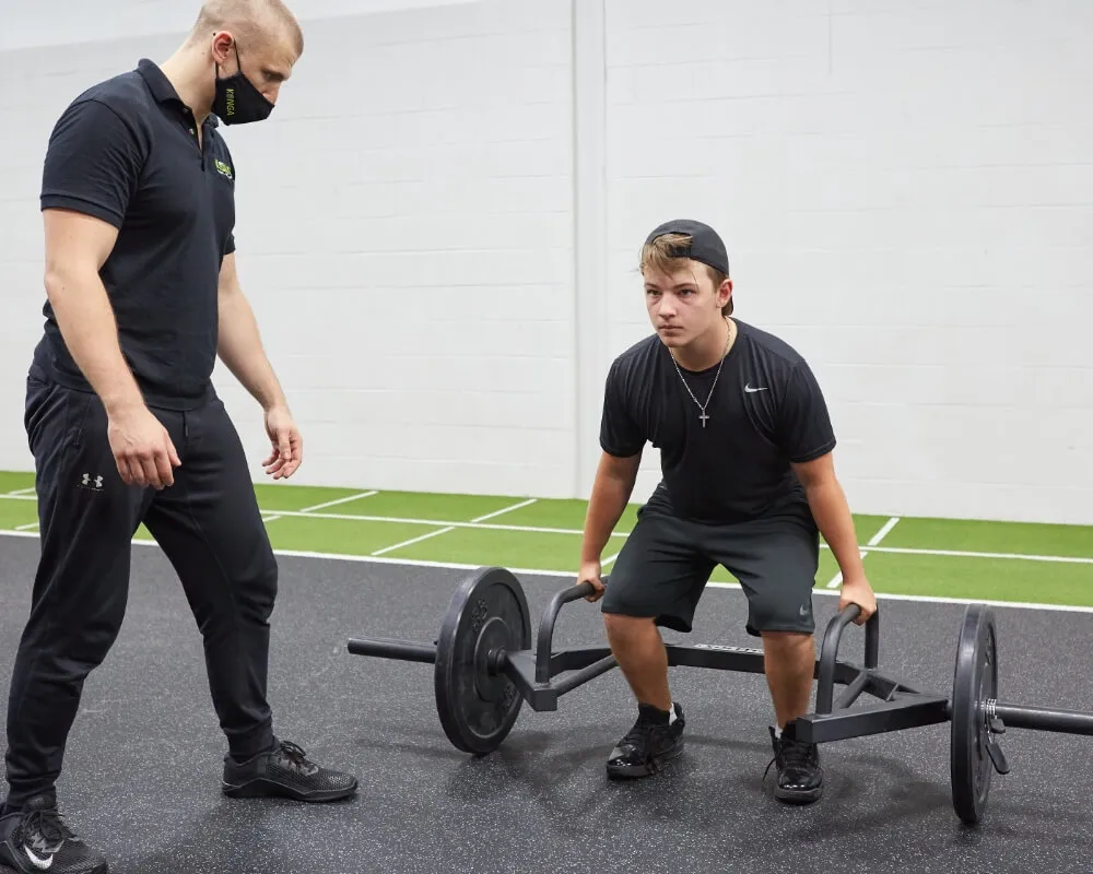 Trainer coaching a member through a trap-bar deadlift