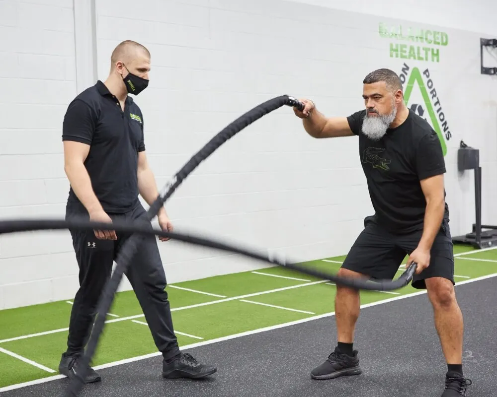 Trainer supervising a member using battle ropes