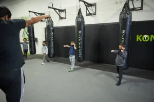 Coach leading children through a martial arts drill beside the punching bags