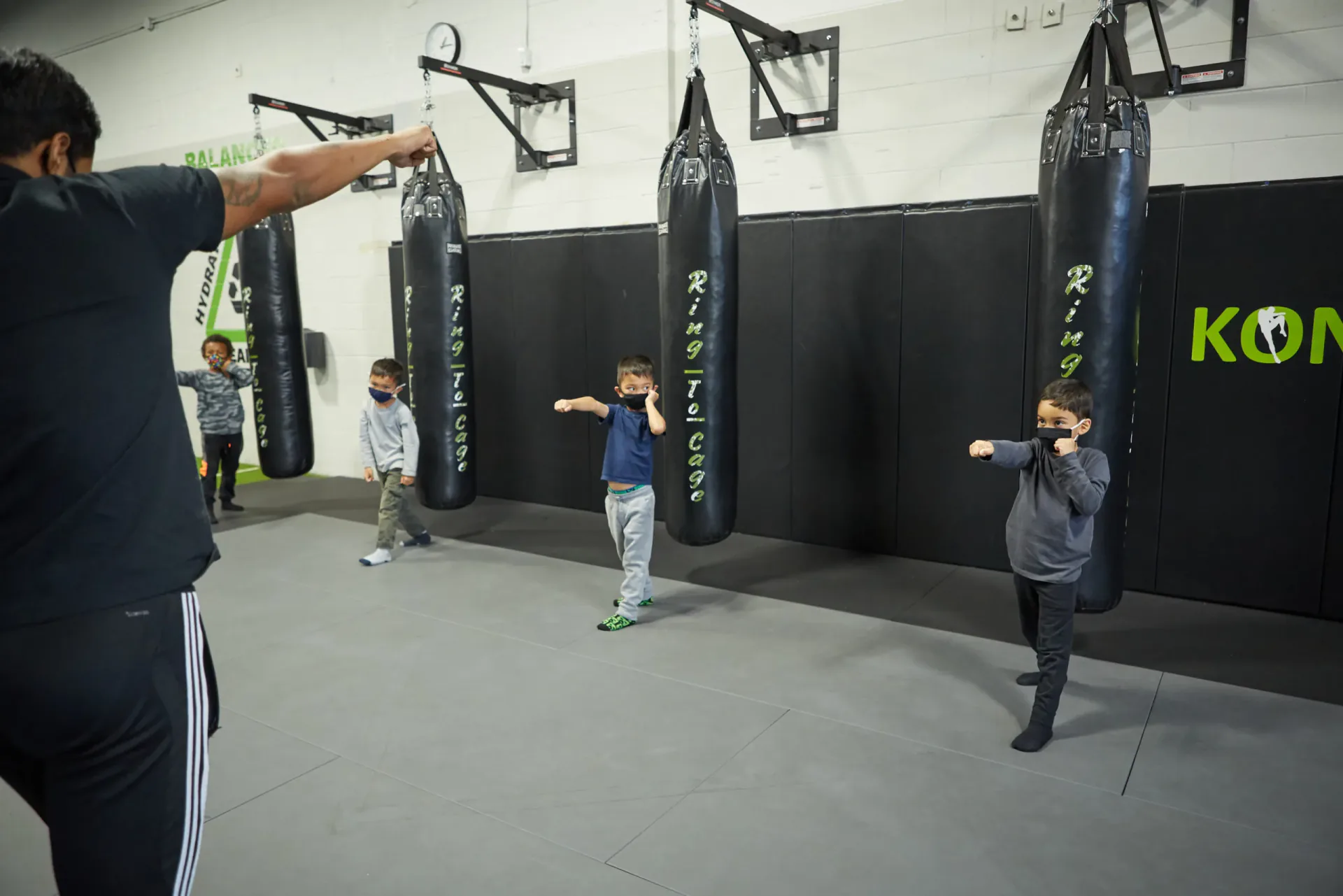 Coach leading children through martial arts drills beside punching bags