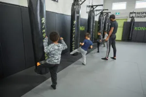 Children practising kicks beside punching bags with a coach