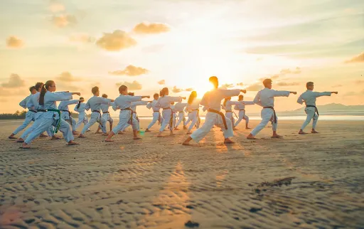 Group practising martial arts together on a beach at sunset