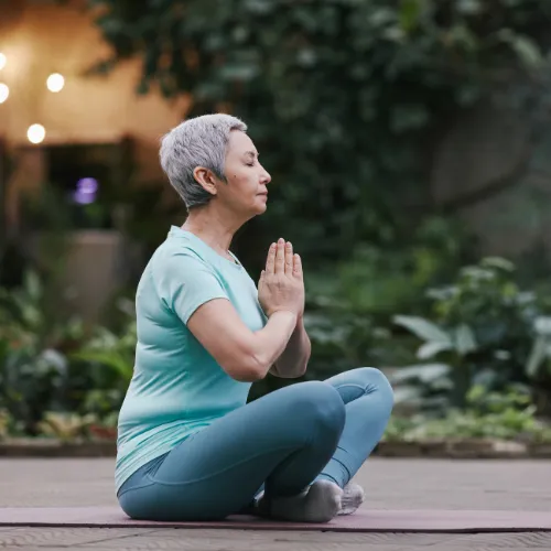 Woman seated cross-legged outdoors with hands together