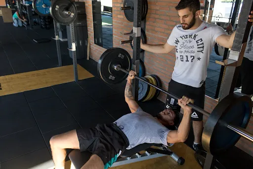 Trainer spotting a member's barbell bench press