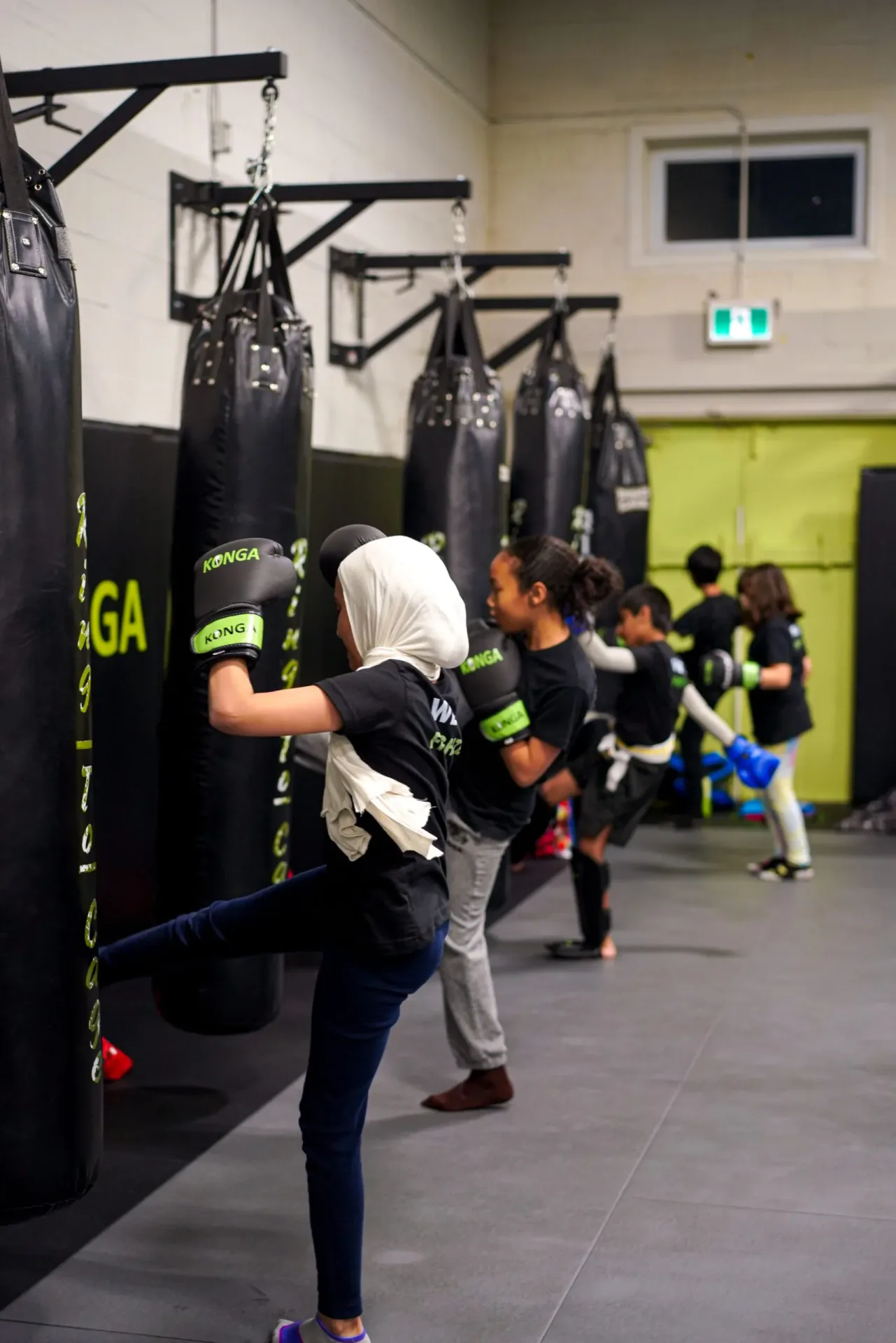 Children practising kicks beside the heavy bags
