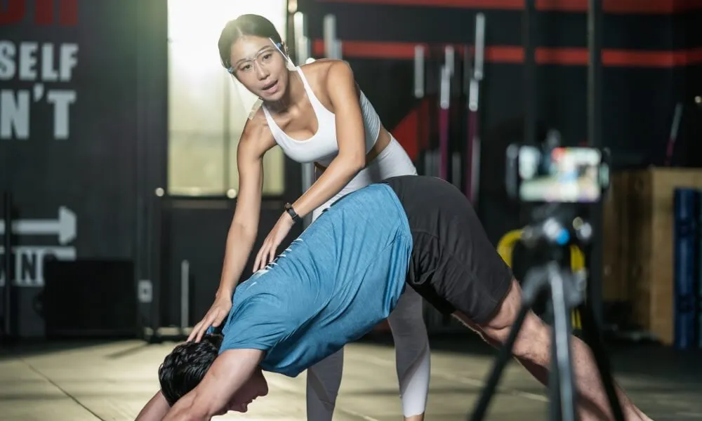 Trainer guiding a client's stretch in a gym