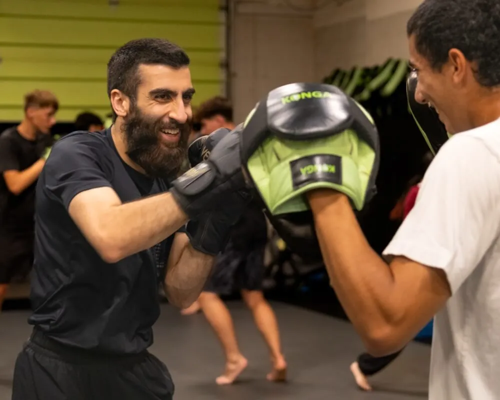 Coach holding focus mitts for a smiling boxing student