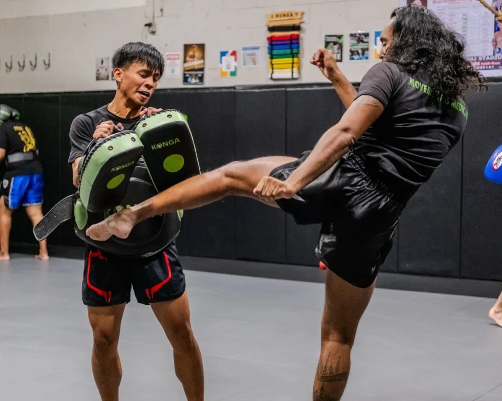 Muay Thai student practising a kick against pads held by a coach