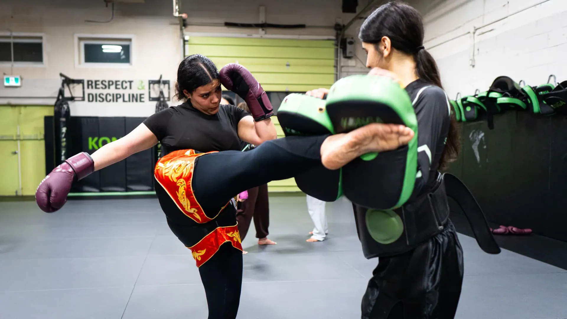 Woman practising a kick against pads held by a training partner
